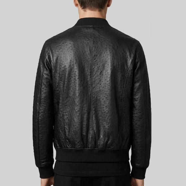 Rear view of a person wearing a black textured leather bomber jacket against a solid gray background.